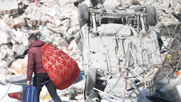 Ein Mann l&auml;uft mit seinen Habseligkeiten &uuml;ber Erdbebentr&uuml;mmer in Antakya. - &copy; Shadati/XinHua/dpa