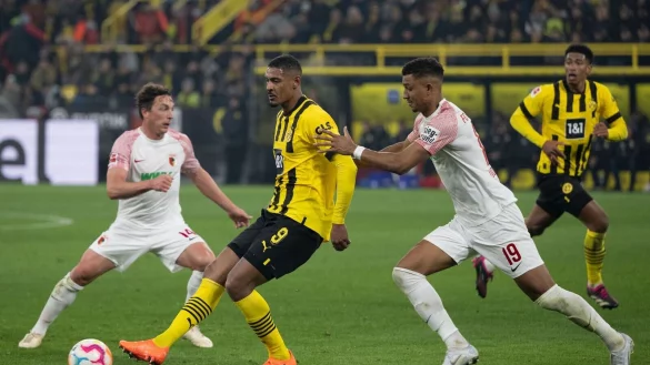 Dortmunds Sebastien Haller und Felix Uduokhai von Augsburg versuchen an den Ball zu kommen. - &copy; Bernd Thissen/dpa