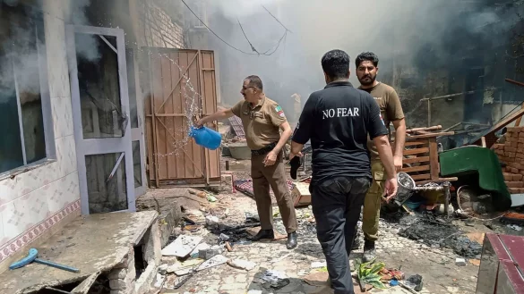 Ein Polizist kippt der Wasser aus einem Gefäß in ein brennendes Gebäude. - © Uncredited/District Police Office/AP/dpa