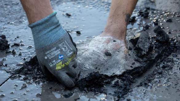 Ein Polizist entfernt Asphalt, um einen Aktivisten von der Straße zu lösen. - © Hannes P. Albert/dpa