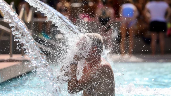 Ein Mann erfrischt sich im Donaubad in Sigmaringen unter einer Wasserfontäne. - © Thomas Warnack/dpa