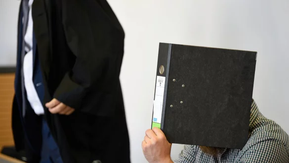 Der Angeklagte verbirgt sein Gesicht vor Gericht hinter einem Aktenordner. - &copy; Frank Hormann/dpa