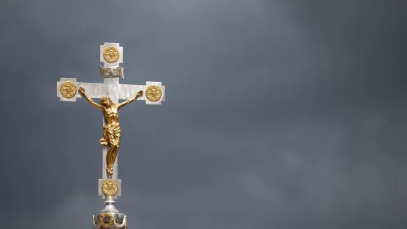 Ein katholisches Kruzifix ist vor dunklen Wolken zu sehen. - © Marijan Murat/dpa/Symbolbild
