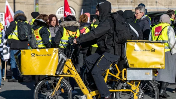 Ein Postbote radelt in Bielefeld an Streikenden einer Verdi-Aktion vorbei (Archivbild). F&uuml;r die Post ist die Gefahr eines unbefristeten Arbeitskampfes noch nicht gebannt. - &copy; David Inderlied/dpa