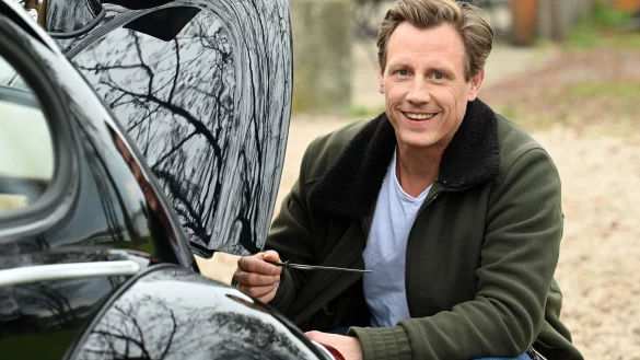 Der Schauspieler Patrick Kalupa hockt bei einem Fototermin an seinem Oldtimer VW K&auml;fer. - &copy; Jonathan Penschek/dpa/Archivbild