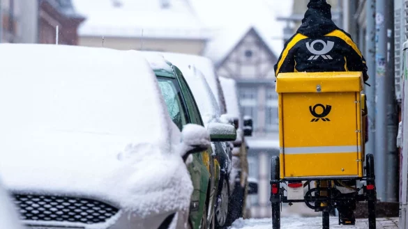 Eine Briefträgerin ist mit ihrem Fahrrad in der Altstadt von Schwerin unterwegs. - © Jens Büttner/dpa