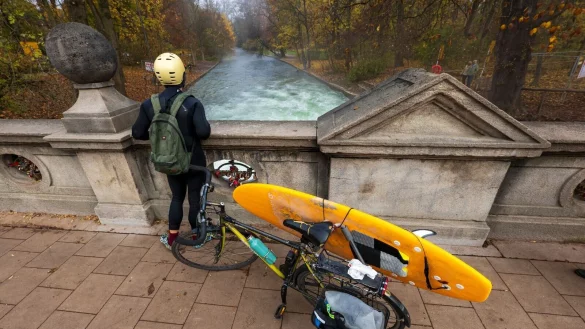 Ein Mann mit einem Surfboard an seinem Fahrrad schaut von einer Br&uuml;cke auf die - nicht mehr vorhandene - Eisbachwelle im Englischen Garten. - &copy; Peter Kneffel/dpa