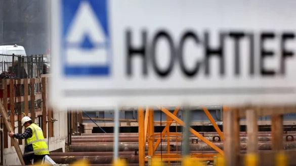 Hinter einem Logo des Baukonzerns Hochtief steigt ein Arbeiter auf einer Baustelle eine Leiter herunter. (Foto Archiv) - &copy; Martin Gerten/dpa
