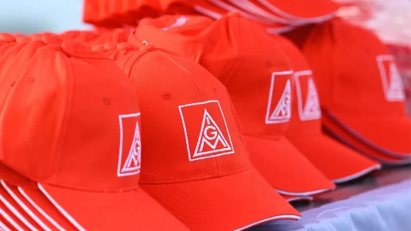 Mützen mit dem Logo der IG Metall liegen auf einem Tisch. - © Heiko Rebsch/dpa/Symbolbild