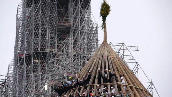 Arbeiter feiern den Abschluss des Wiederaufbaus des Dachstuhls der Kathedrale Notre Dame mit einem traditionellen Blumenstrau&szlig;. - &copy; Christophe Ena/AP/dpa
