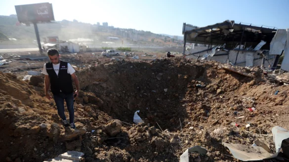 Ein libanesischer Polizist steht in der N&auml;he eines Kraters nach einem israelischen Luftangriff auf einen Hangar im S&uuml;dlibanon. - &copy; Mohammed Zaatari/AP/dpa