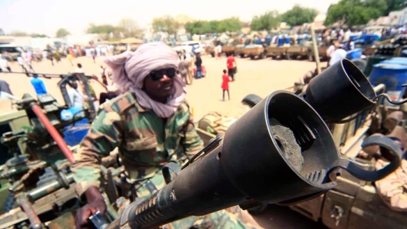 Ein Milizion&auml;r sitzt neben milit&auml;rischer Ausr&uuml;stung, die angeblich w&auml;hrend eines Gefechts im umk&auml;mpften Gebiet in S&uuml;d-Darfur erbeutet wurde. - &copy; Marwan Ali/EPA/dpa