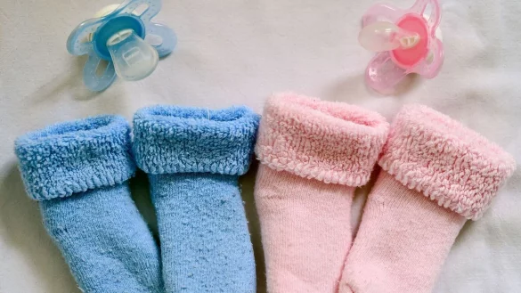 Rosa und blaue S&ouml;ckchen und dazu die farbigen Nuckel liegen in einem Babybett. - &copy; Patrick Pleul/dpa-Zentralbild/dpa/Illustriert