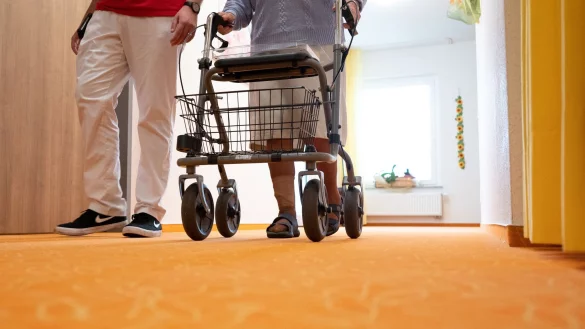 Ein Betreuer geht in einem Pflegeheim mit einer Bewohnerin &uuml;ber den Flur. - &copy; Bernd Wei&szlig;brod/dpa/Symbolbild