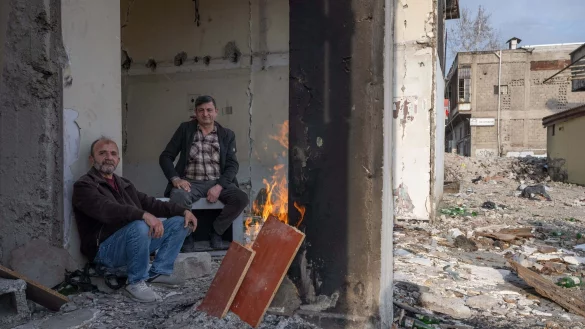 Zwei M&auml;nner w&auml;rmen sich in den Tr&uuml;mmern eines zerst&ouml;rten Hauses in Kahramanmaras an einem Feuer. Im Zentrum der Stadt waren bei dem Beben vor einem Jahr unz&auml;hlige H&auml;user zerst&ouml;rt oder besch&auml;digt worden. - &copy; Boris Roessler/dpa