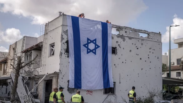 Eine riesige israelische Fahne hängt vom Dach eines beschädigten Gebäudes in Kiriat Bialik. - © Ilia Yefimovich/dpa