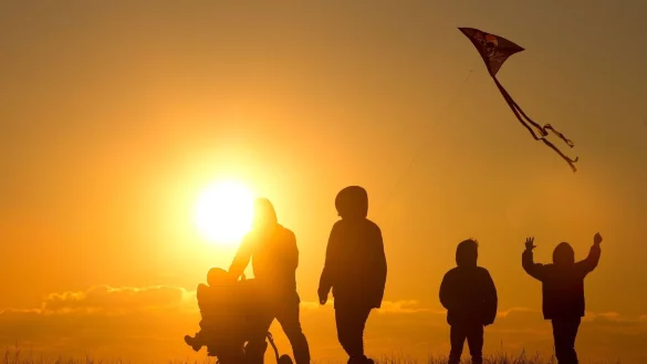 Eine Familie mit Kinderwagen und Drachen im Schlepptau geht bei Sonnenuntergang &uuml;ber einen Weg. - &copy; Christian Charisius/dpa