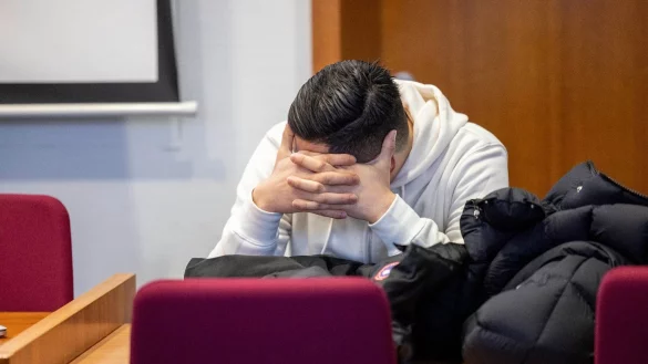 Einer der sieben Angeklagten verdeckt sein Gesicht im Gerichtssaal vor Beginn des Prozesses. - &copy; Thomas Banneyer/dpa