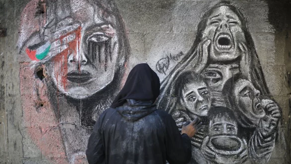 Eine palästinensische Künstlerin bemalt mit Kohle die Wände einer Schule in Deir al-Balah im Zentrum des Gazastreifens, in die sie umgesiedelt wurde. - © Mohammed Talatene/dpa