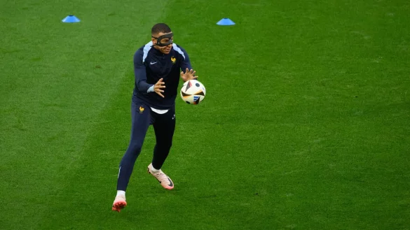 Frankreichs Kylian Mbappe steht w&auml;hrend der Erw&auml;rmung mit einer Schutzmaske nach seinem Nasenbeinbruch auf dem Feld. - &copy; Robert Michael/dpa