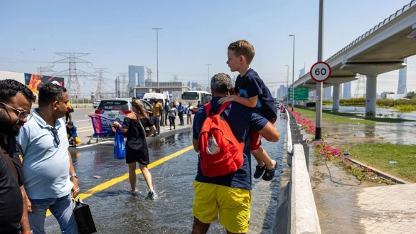 Ein Mann tr&auml;gt ein Kind durch das von starkem Regen verursachte Hochwasser in Dubai. - &copy; Christopher Pike/AP/dpa