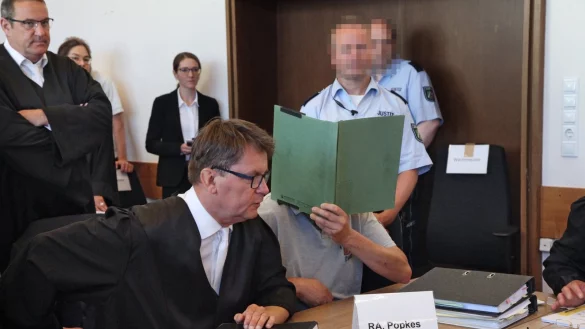 Der Angeklagte Heiko V. verbirgt sein Gesicht hinter einem Aktendeckel. Neben ihm sitzt sein Verteidiger Jann Popkes. Links dahinter ist der Nebenklagevertreter eines Opfers Roman von Alvensleben zu sehen. - © Bernhard Preuß