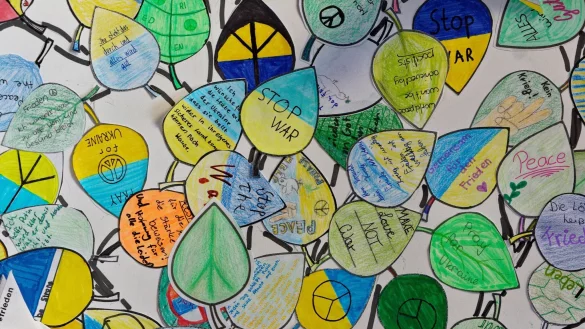 Aufschriften auf Bl&auml;ttern in einem Bild im Eingangsbereich eines Gymnasiums w&uuml;nschen Frieden. - &copy; Henning Kaiser/dpa