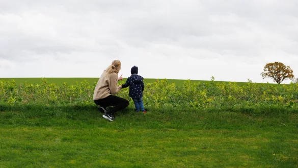 Julia Trienens blickt mit ihrem Kind auf eine Wiese in der Umgebung ihres Wohnhauses. - &copy; Friso Gentsch/dpa