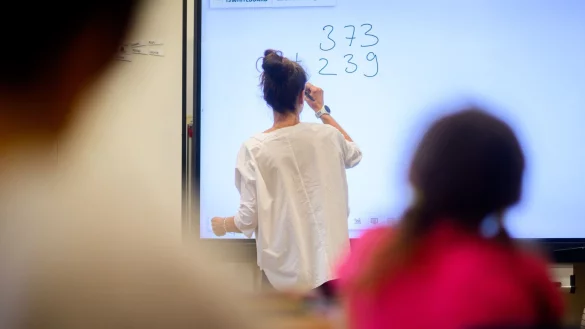 Eine Lehrerin schreibt eine Mathematikaufgabe auf eine digitale Schultafel im Klassenraum einer 4. Klasse einer Grundschule. - © Julian Stratenschulte/dpa