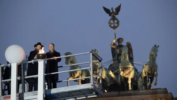 Rabbiner Yehuda Teichtal (l.) und Bundeskanzler Olaf Scholz zünden beim traditionellen zentralen Chanukka-Lichterzünden am Brandenburger Tor in Berlin ein Licht an. - © Sebastian Christoph Gollnow/dpa