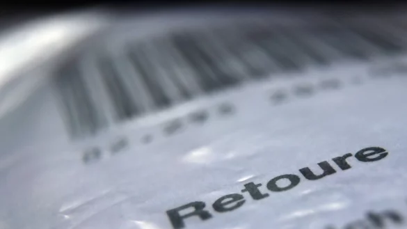 Das Wort «Retoure» steht auf dem Retourenaufkleber eines in Folie verpackten Päckchens. - © Karl-Josef Hildenbrand/dpa