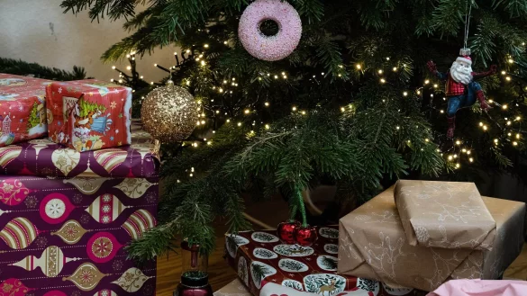 Eingepackte Geschenke liegen unter einem geschmückten Weihnachtsbaum. Die Menschen in Deutschland wollen in diesem Jahr bei den Präsenten sparsamer sein. - © Swen Pförtner/dpa