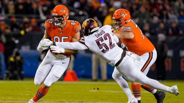 Chicagos Tight End Cole Kmet (l) wird von Washingtons Linebacker Jamin Davis (M) angegangen. - &copy; Nam Y. Huh/AP/dpa