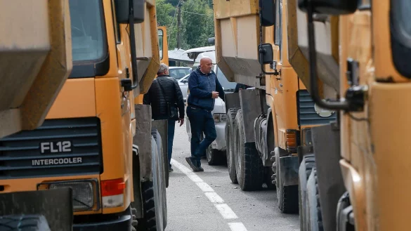 Zwei serbische M&auml;nner stehen neben einer Stra&szlig;e, die zum Grenz&uuml;bergang Jarinje im Norden des Kosovo f&uuml;hrt. - &copy; Visar Kryeziu/AP/dpa