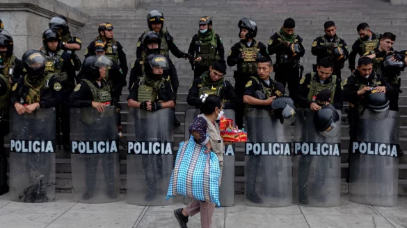 Gegens&auml;tze in Perus Hauptstadt Lima: Eine Frau l&auml;uft mit S&uuml;&szlig;igkeiten in der Hand an einer mit Schutzschilden und Helmen ausgestatteten Gruppe von Polizisten vor&uuml;ber. - &copy; Lucas Aguayo Araos/dpa