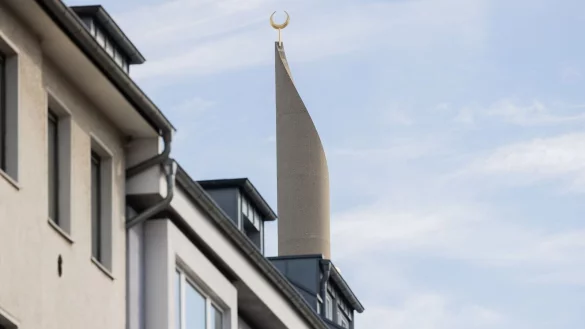 Ein Minarett der Zentralmoschee der DITIB ragt hinter Wohnhäusern im Stadtteil Ehrenfeld in den Himmel. - © Rolf Vennenbernd/dpa