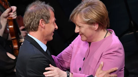 Der ehemalige Bundestrainer Jürgen Klinsmann und die frühere Bundeskanzlerin Angela Merkel (CDU) umarmen sich bei einem Festakt im Jahr 2016. - © Martin Schutt/dpa