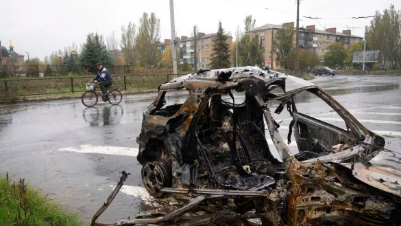 Ein Mann fährt in Bachmut mit seinem Fahrrad an einem Auto vorbei, das durch Beschuss zerstört wurde. - © Efrem Lukatsky/AP/dpa
