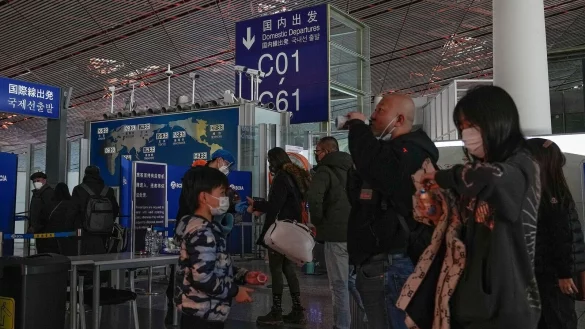 Passagiere mit Mund-Nasen-Schutz stehen am Flughafen Peking an der Sicherheitskontrolle vor einem internationalen Abfluggate an. - &copy; Andy Wong/AP/dpa