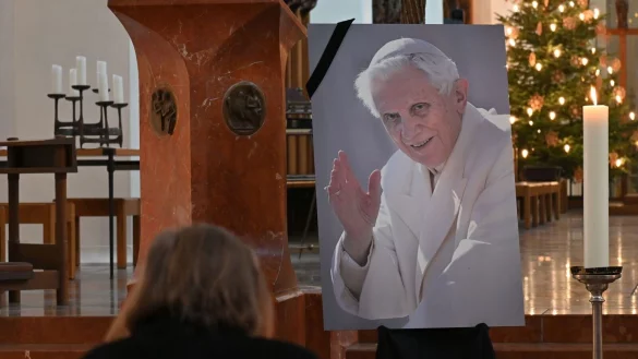 Eine Frau betet in der Frauenkirche in M&uuml;nchen vor einem Bild des verstorbenen emeritierten Papst Benedikt XVI. - &copy; Katrin Requadt/dpa