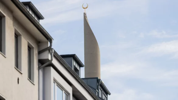 Ein Minarett der Zentralmoschee der DITIB ragt hinter Wohnhäusern in den Himmel. - © Rolf Vennenbernd/dpa