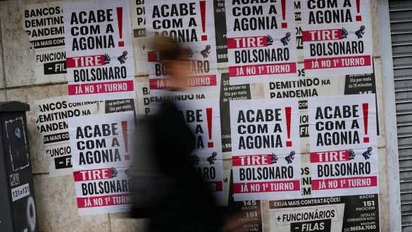 Eine Frau geht in Rio De Janeiro an Schildern vorbei, auf denen auf portugiesisch zu lesen ist: «Schluss mit der Agonie, Bolsonaro raus». - © Matias Delacroix/AP/dpa
