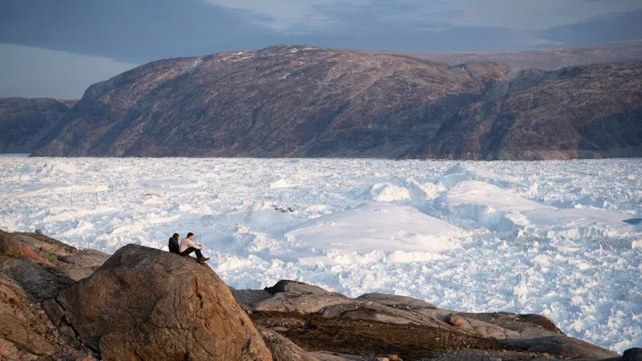 Zwei Studenten der New York University sitzen auf einem Felsen mit Blick auf den grönländischen Helheim-Gletscher. - © Felipe Dana/AP/dpa