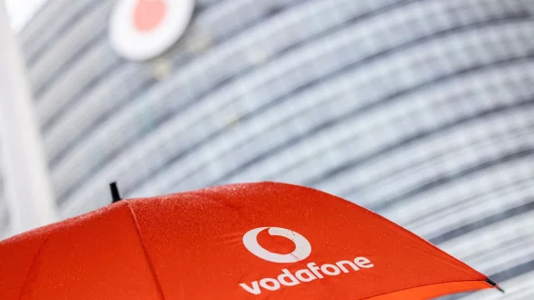 Ein Passant geht mit einem aufgespanntem Regenschirm mit dem Logo von Vodafone an der Zentrale der Deutschlandtochter des britischen Vodafone-Konzerns vorbei. - &copy; Thomas Banneyer/dpa