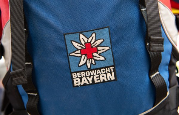 Das Logo der Bergwacht ist an einem Rucksack zu sehen. Bei Oberstdorf musste die Bergwacht nun einen Mann retten, der ohne richtige Ausrüstung und Erfahrung zwei Nächte in den Bergen verbrachte. (Archivfoto-Illustration) - © Sven Hoppe/dpa