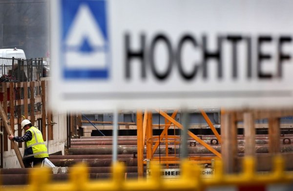 Hinter einem Logo des Baukonzerns Hochtief steigt ein Arbeiter auf einer Baustelle eine Leiter herunter. (Foto Archiv) - © Martin Gerten/dpa