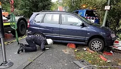 Ein Feuerwehrmann spricht mit Andreas Klein, der unter dem Opel Zafira gefangen ist. Die orangefarbene Arbeitskleidung des Elektrikers der Bielefelder Stadtwerke ist durch den schmalen Spalt unter dem Auto zu sehen. - &copy; FOTO: WOLFGANG RUDOLF