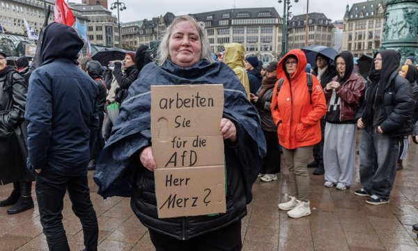 Eine Demonstrantin in Hamburg stellt auf einem Pappschild eine Frage an Bundeskanzler Friedrich Merz (CDU). - © Markus Scholz/dpa