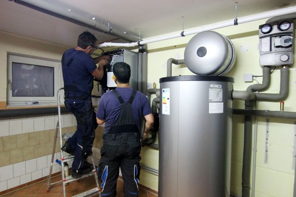 Zwei Handwerker stellen eine gerade installierte Wärmepumpe im Keller einer Doppelhaushälfte ein. - © Doreen Garud/dpa