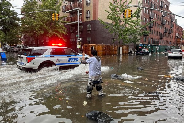 Hochwasser auf den Straßen von New York: Im Stadtteil Brooklyn versucht ein Mann, mit einem Stock einen Abfluss zu reinigen, während ein Polizeiwagen vorbeifährt. - © Jake Offenhartz/AP/dpa